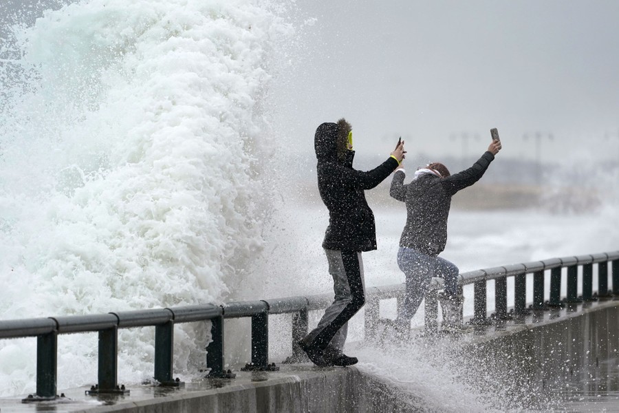 Two women jump as a large wave splashes behind them.
