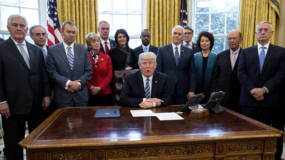 Donald Trump at his desk surrounded by people, including Mike Pence