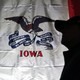 The Iowa state flag hangs at a rally site at the University of Iowa in Iowa City. A person, in shadow and wearing a baseball cap, stands in front of it.