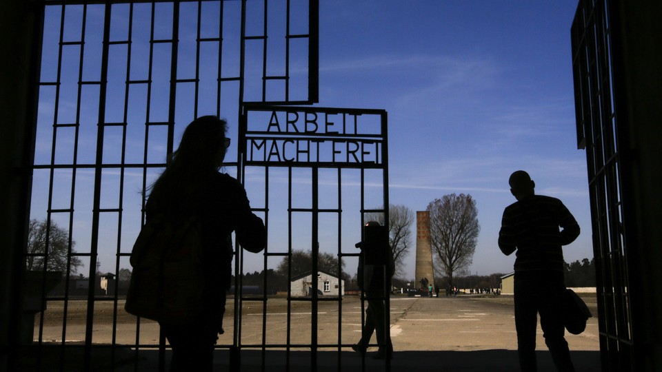 Visitors enter Sachsenhausen through a gate with the words "Arbeit macht frei" (works sets you free).