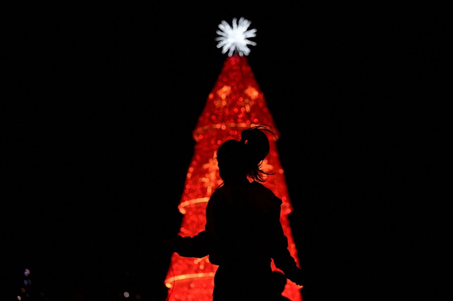 A woman jumps rope in front of a Christmas tree in a city square.