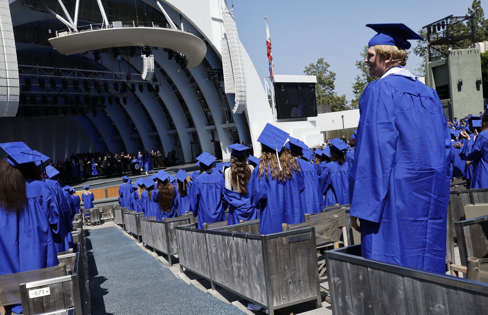 Graduating high school students in caps and gowns stand in the audience section of the Hollywood Bowl.