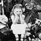 A girl sits with her face in her hands, looking disgruntled, surrounded by gifts under a Christmas tree