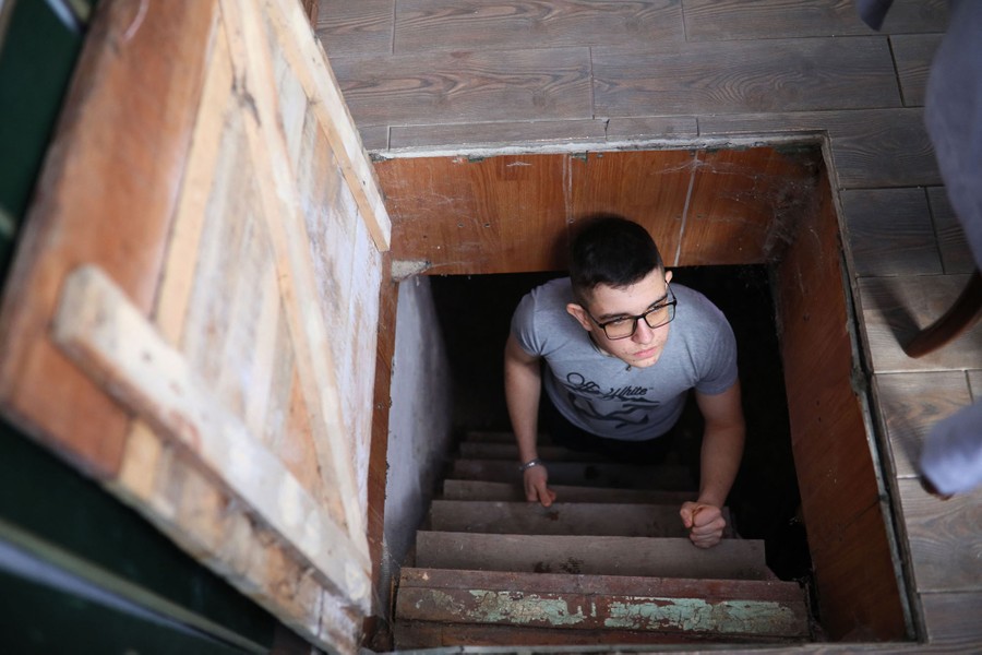 A teenager stands in a stairwell beneath a trap-door entrance.