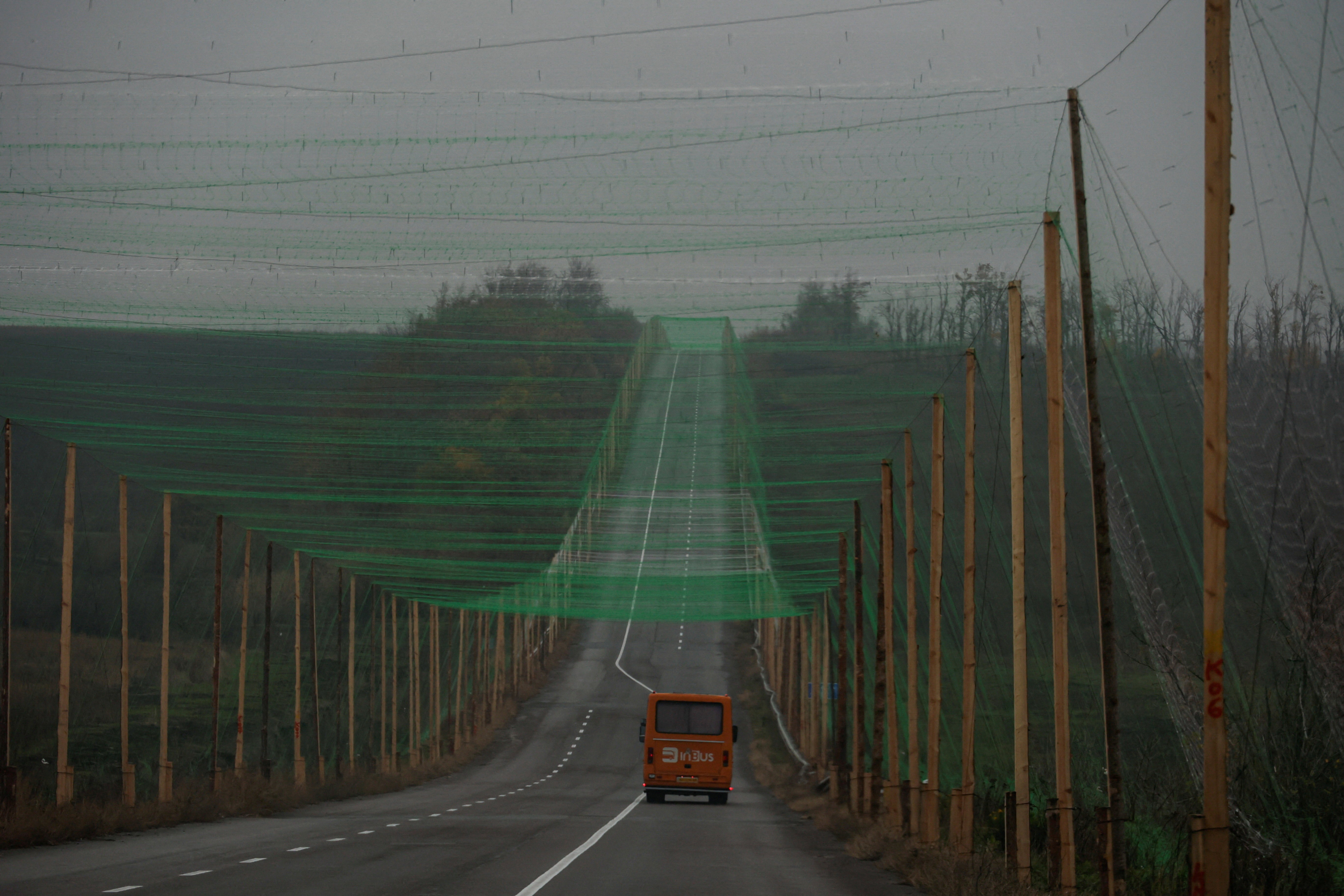 A car drives along a road covered with anti-drone netting, supported by tall poles on either side of the road.