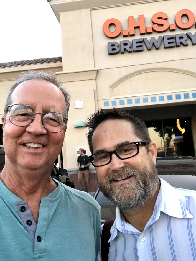 Two men smile in front of a building with a sign that reads "O.H.S.O. Brewery"