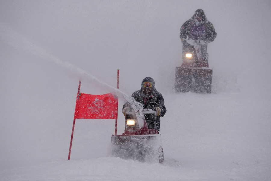 Two people with snowblowers work on a ski course during a snowstorm.