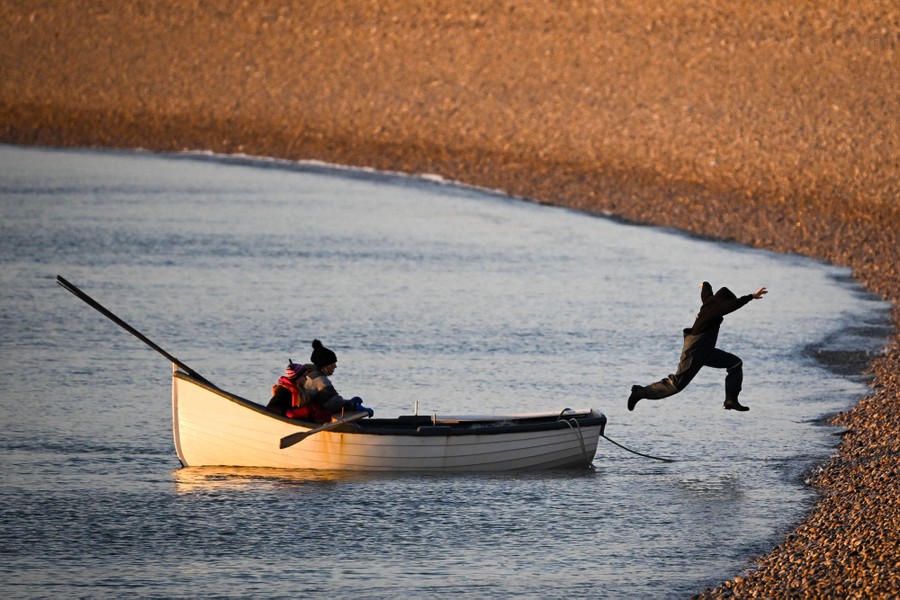 A child leaps from a small boat toward a pebble beach.
