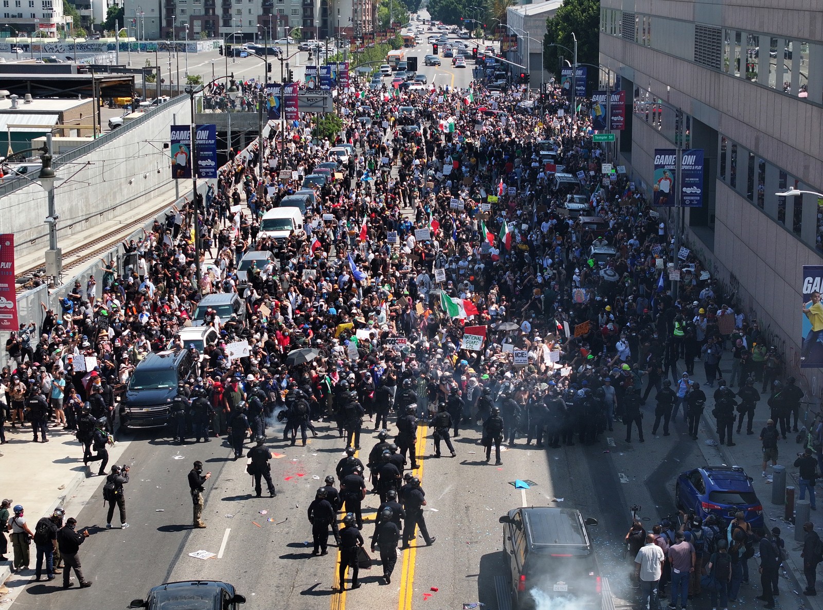 Hundreds of protesters march in a street, confronted by a line of riot police.