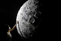 A person reaches up to touch the side of a large-scale model of the moon