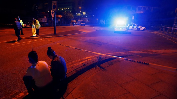 People sit by the side of the road next to a police cordon outside the Manchester Arena.