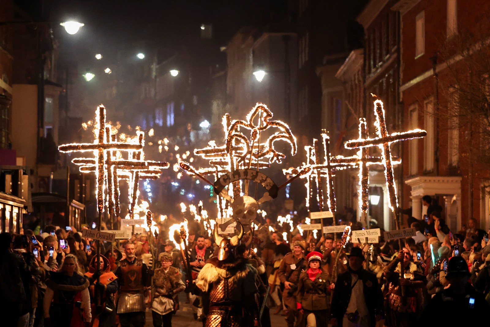 Participants holding cross-shaped torches parade through a town.