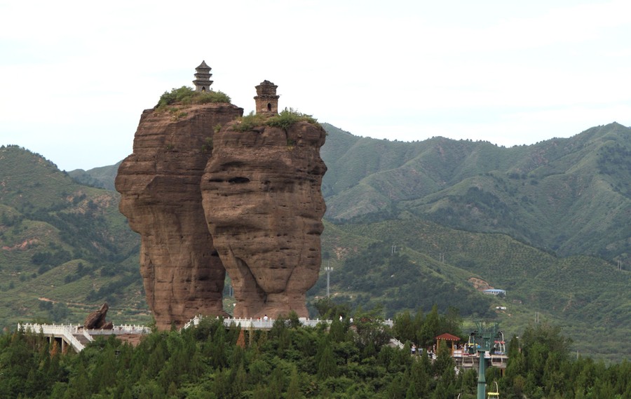 Pagodas stand atop two tall pillars of stone in a forested valley.
