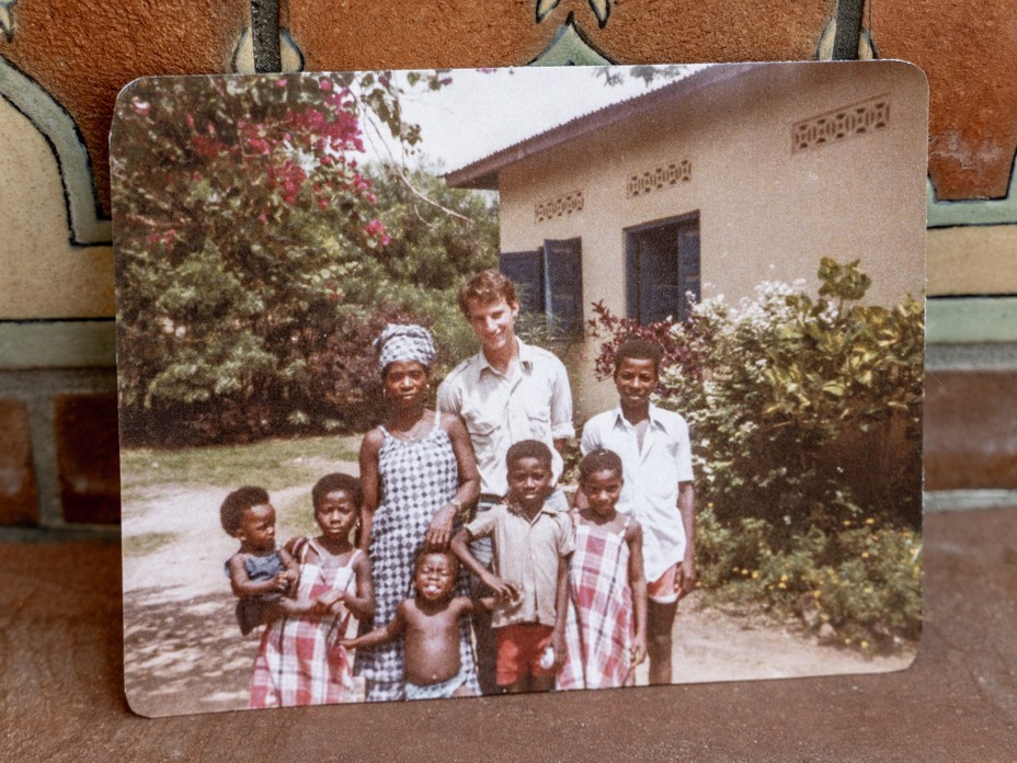 photo of candid color snapshot of tall man standing with woman and half a dozen children in front of building with doors open and flowering trees
