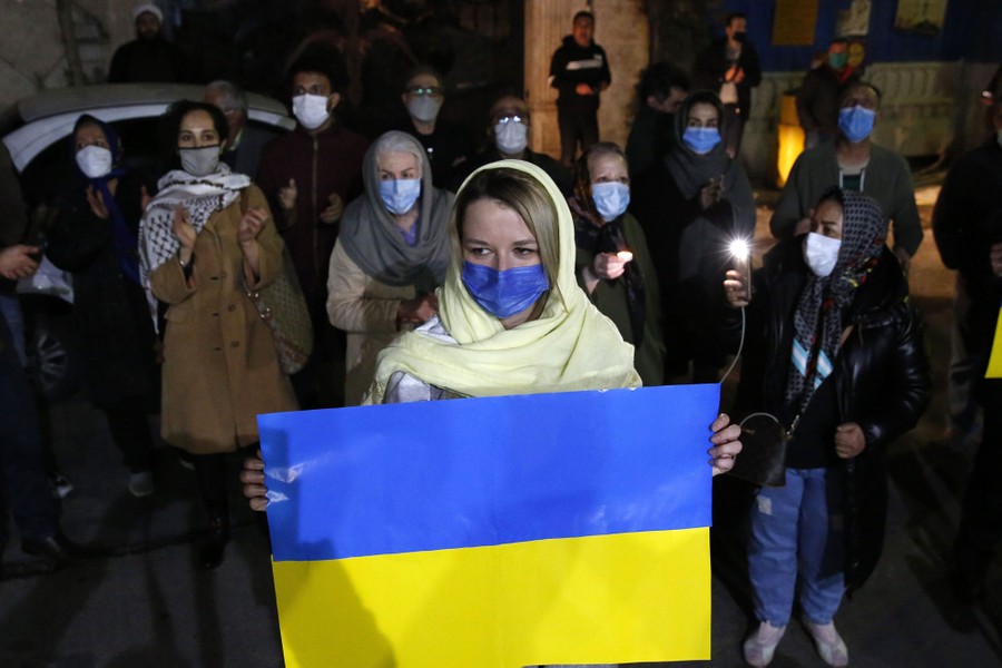 A small crowd of people stand together in a street holding lights and a Ukrainian flag.
