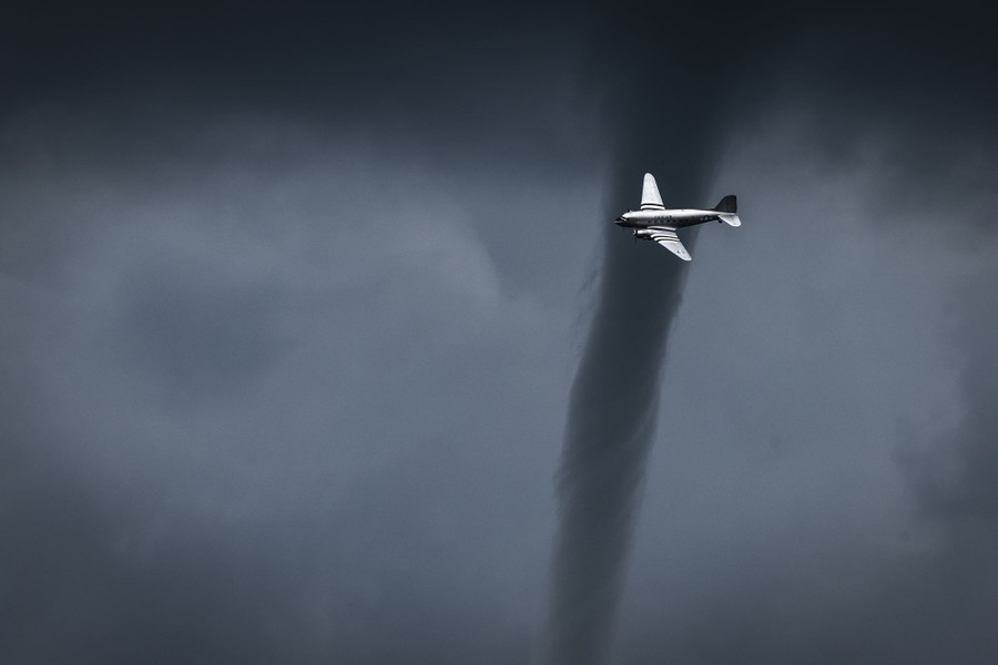 A small tornado forms behind an airplane that flies past.