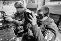 In a black-and-white photo, two men sit at a table operating drones.