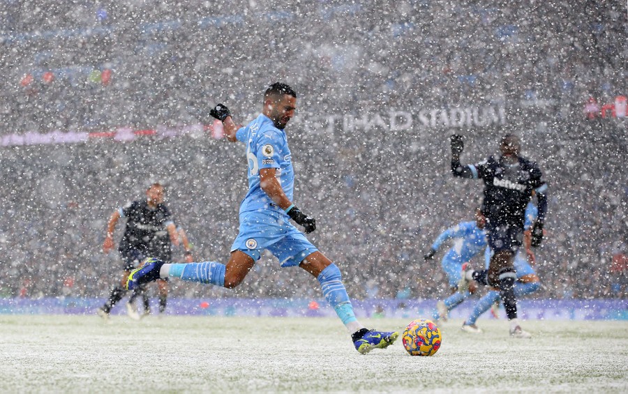 Soccer players compete on a field during a snowstorm.