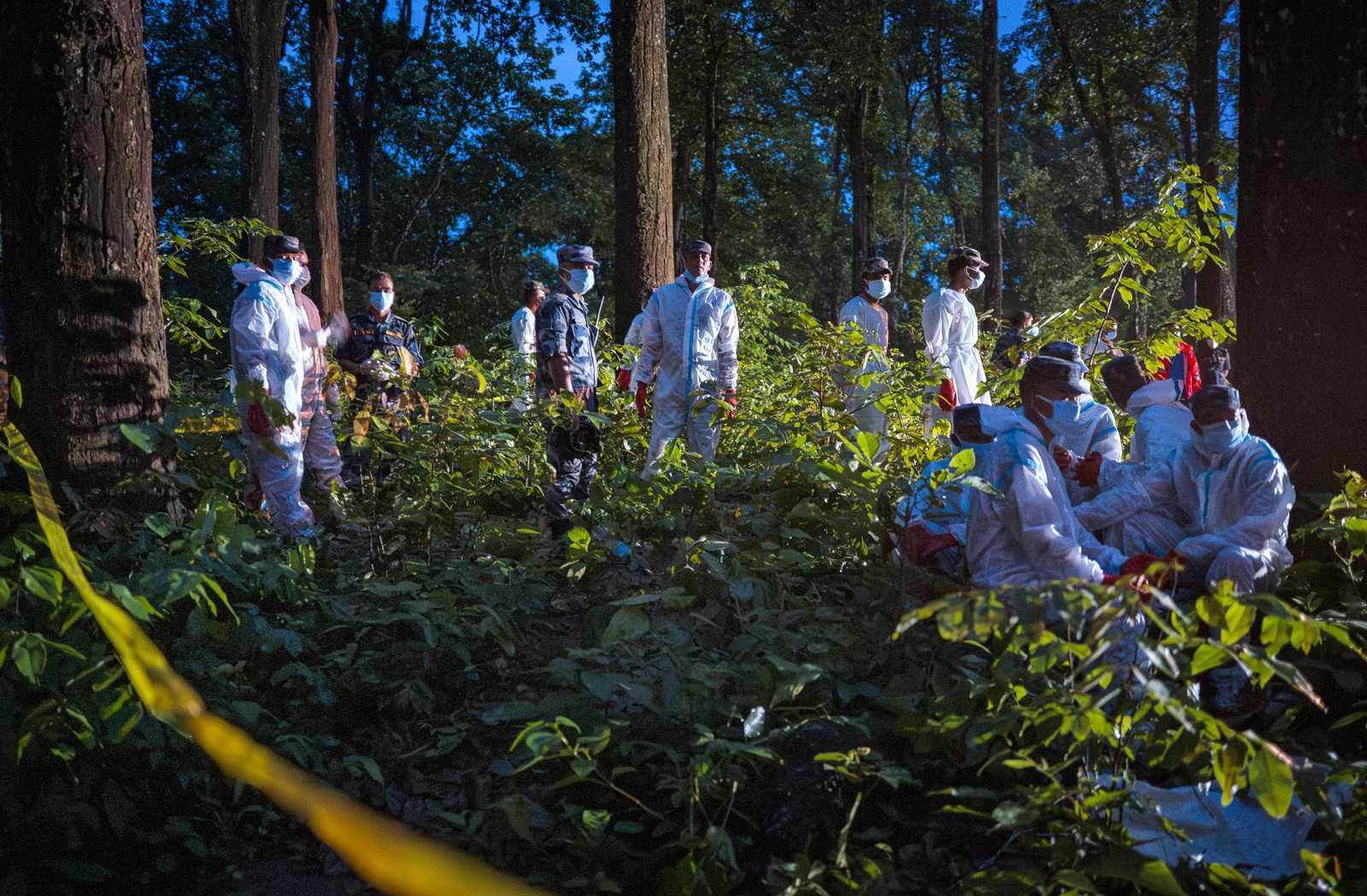 Personnel in hazmat gear in a forest work during a mass burial operation.