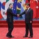 Director-General of the World Trade Organization Roberto Azevêdo shakes hands with Chinese President Xi Jinping on a red stage in front of several countries' flags at the G20 Summit in 2015.