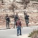 A man faces three armed Israeli soldiers on a road.