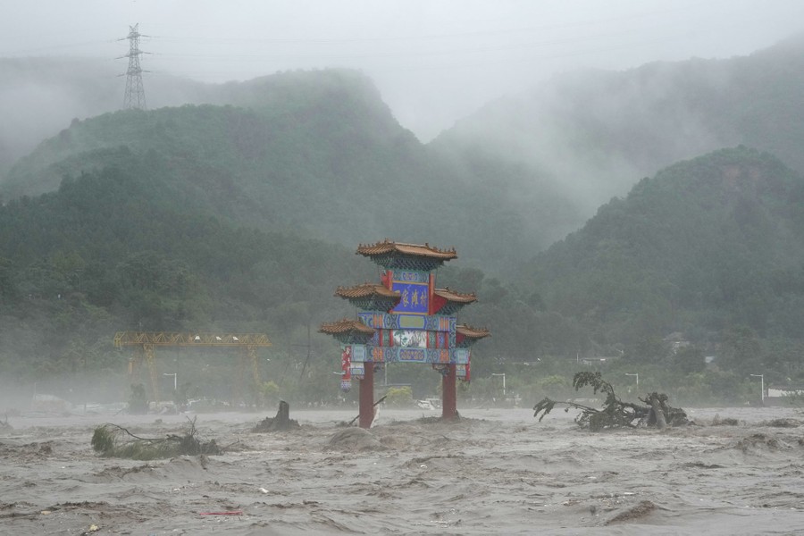 A traditional Chinese gate structure is seen inundated by rushing floodwater.
