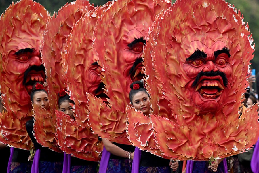 A line of performers hold up large demonic heads during a parade.