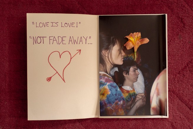 photo of hand-written card with words 'LOVE IS LOVE' AND 'NOT FADE AWAY' alongside heart with arrow on left page and photo of people with flower on right 