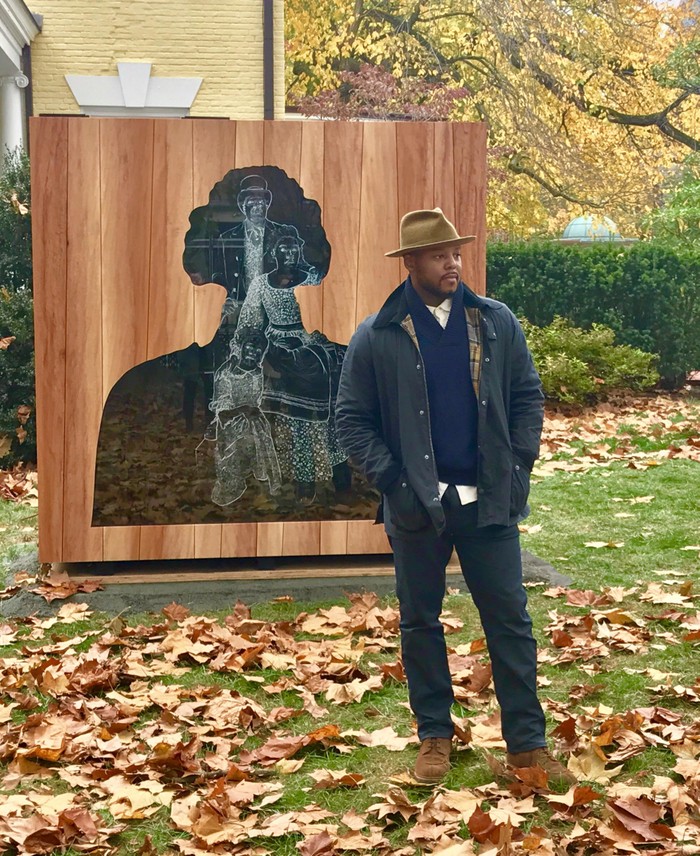The artist Titus Kaphar stands next to the sculpture he created, outside of a Princeton University campus building. 