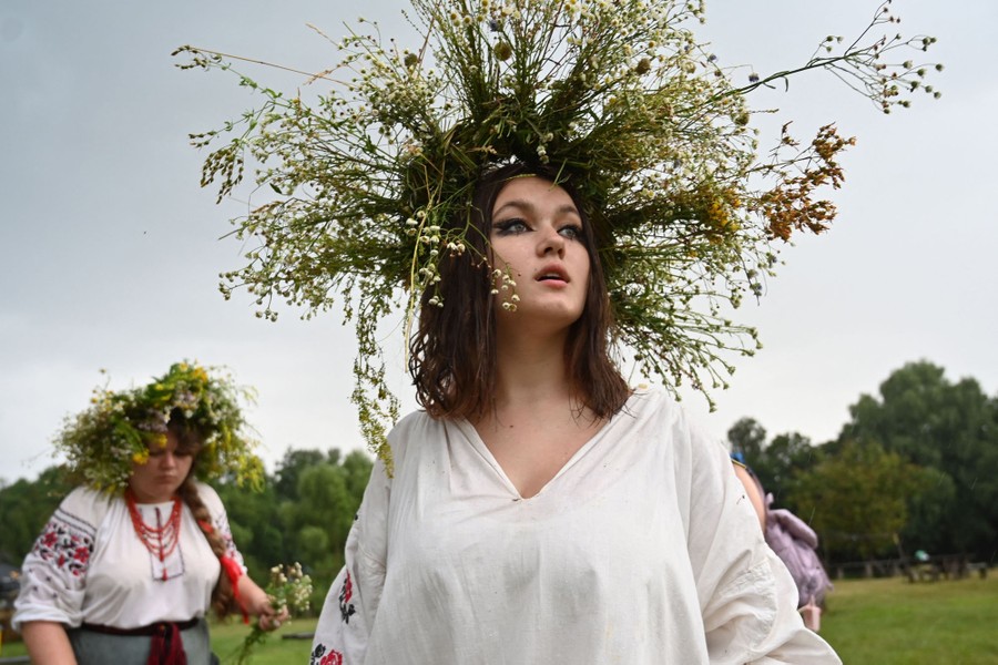 A woman walks in an open space outside, wearing a large wreath of flowers on her head.