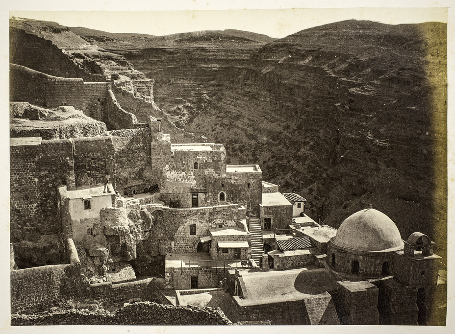 vintage photo of stone buildings, walls, and domed church on cliff with valley behind