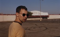 Jack Antonoff in a yellow shirt and sunglasses standing in a parking lot