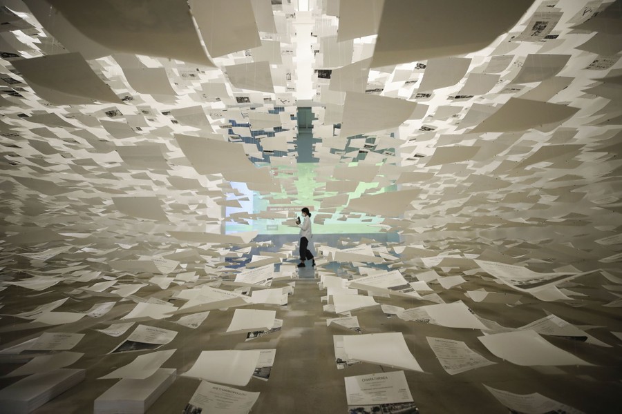 A person walks past an art exhibit featuring hundreds of suspended sheets of paper.