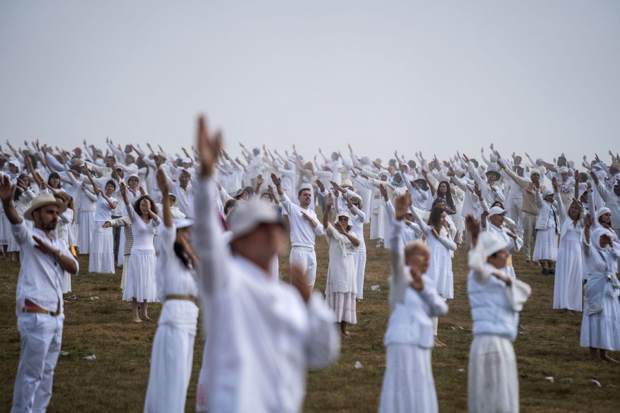 A large group of people wearing white perform movements on a hillside.