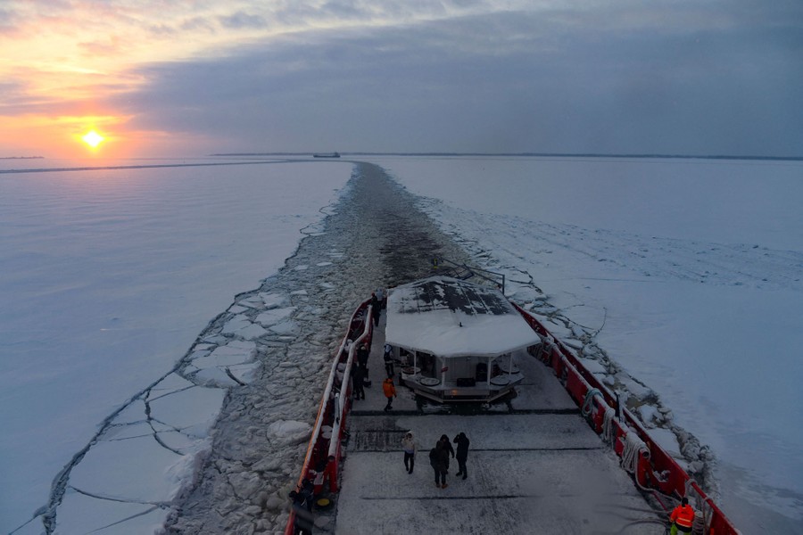 A view of the sunrise from the deck of a ship sailing through a narrow channel cut through ice.