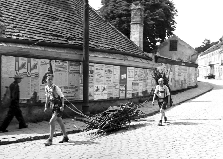 Two civilians wearing lederhosen carry bundles of wood through a street in Vienna, Austria, in July of 1945.