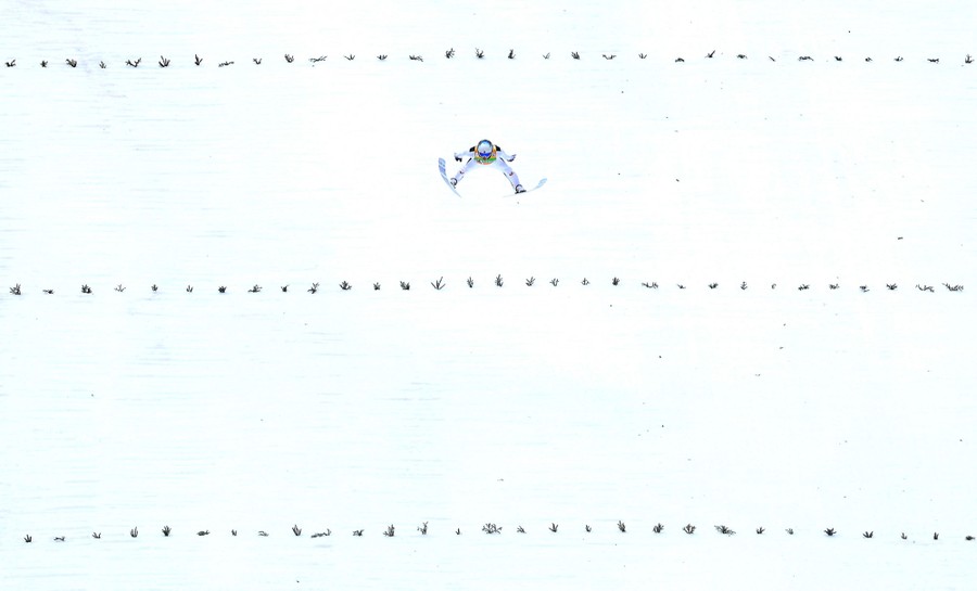 A ski jumper mid-jump, above a snow-covered hill