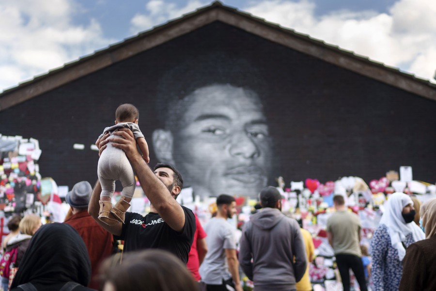 People gather beside a large mural of a soccer player.