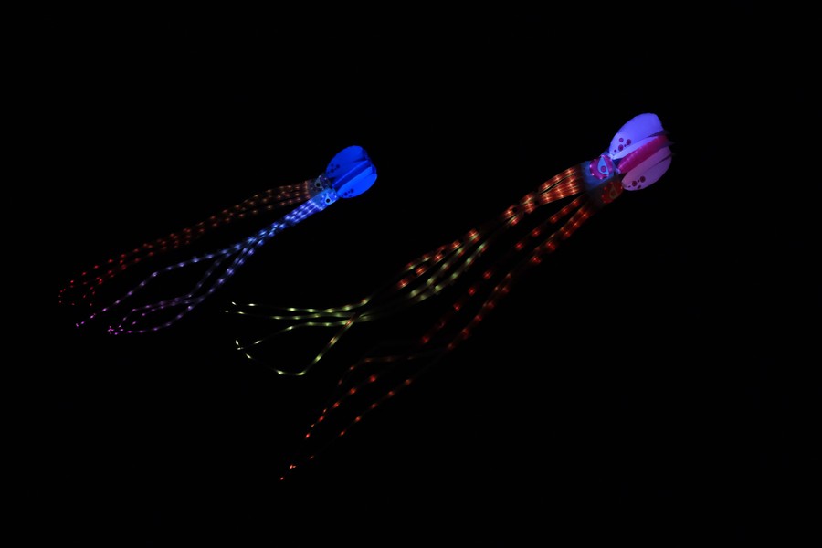 Two illuminated kites shaped like jellyfish fly in a dark sky.