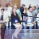 Close-up of microphone and transparent lectern with audience seen in blurred background