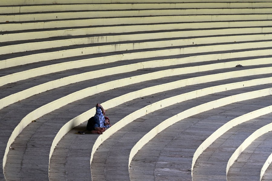 A person naps on curved stadium benches.
