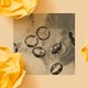 A black-and-white photo shows several shiny wedding bands displayed on a marbled surface.
