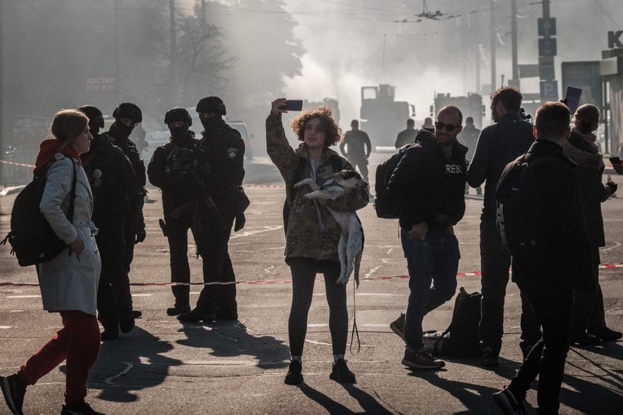 A resident takes a picture in a street after a drone attack, with smoke hanging in the air in the background.