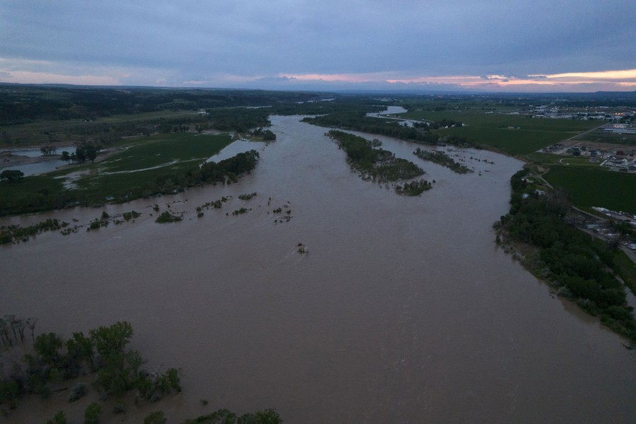 An aerial view of a flooded river on a broad plain of trees and farms.