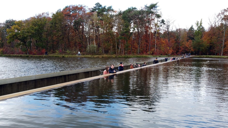 People walk on a path that dips low into a pond.