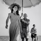 A photograph of Francoise Gilot walking on the beach ahead of Pablo Picasso, who is holding a sun umbrella
