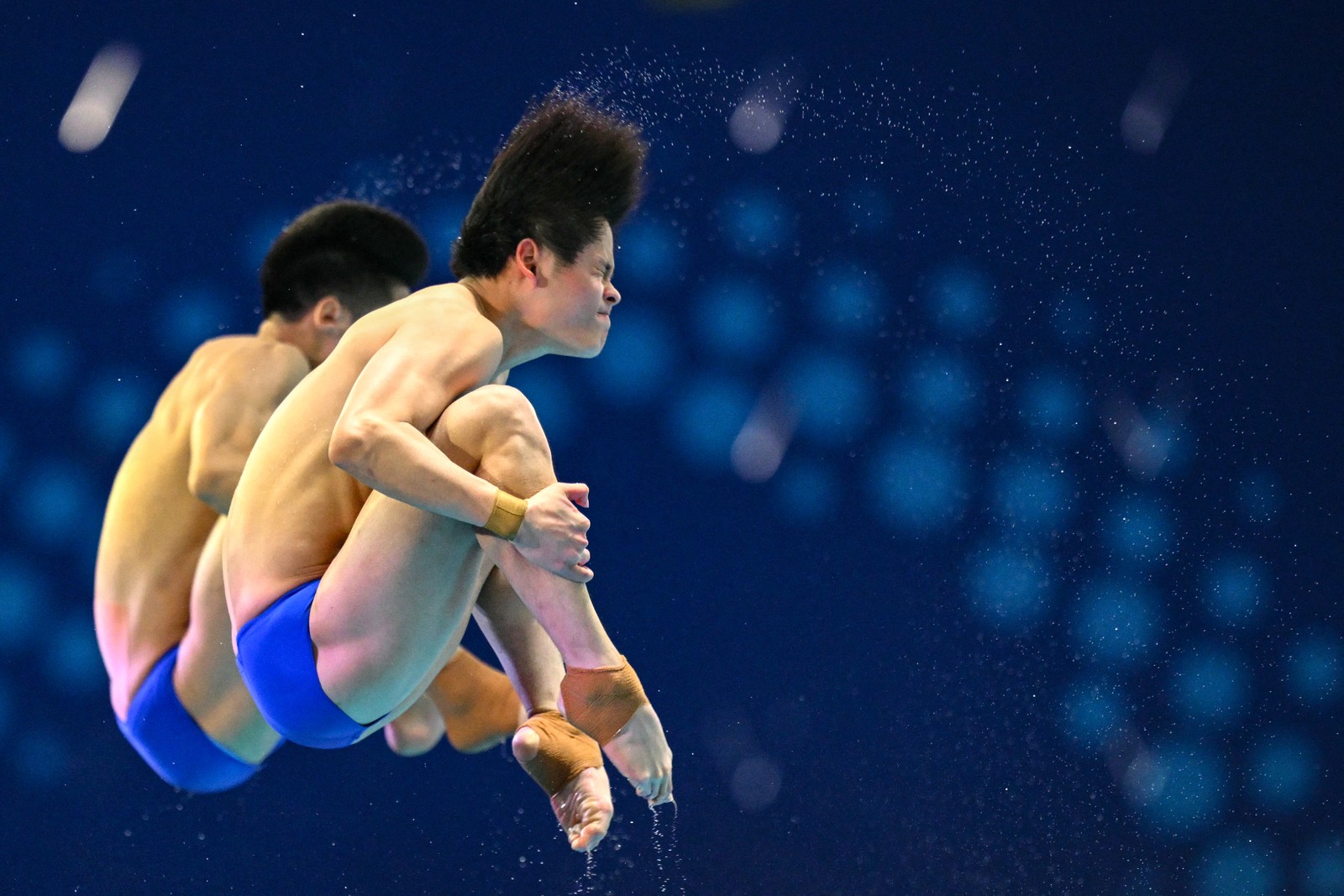 A pair of synchronized divers tucks and rolls during a dive.