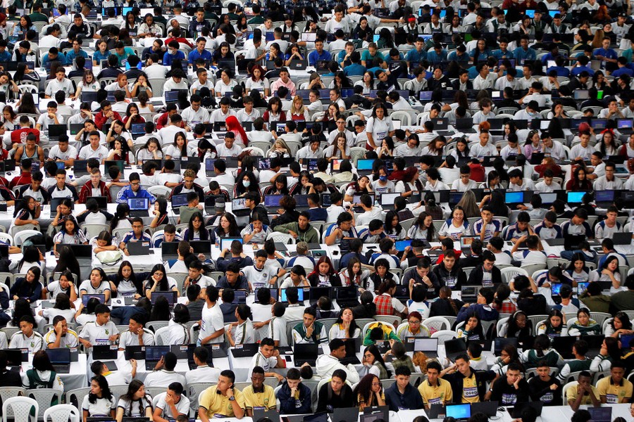 Rows and rows of hundreds of students sit at tables with open laptops.
