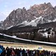 A luge rider races on a curving ice track in a resort town beneath a towering mountain.