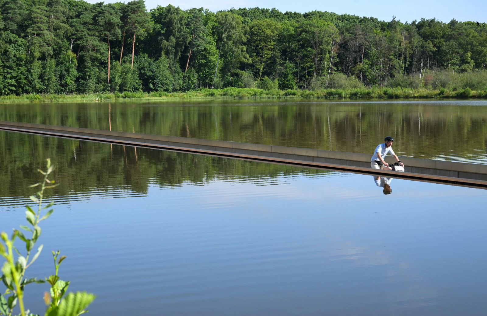 A person rides a bicycle on a path that has been partially submerged in a calm lake.